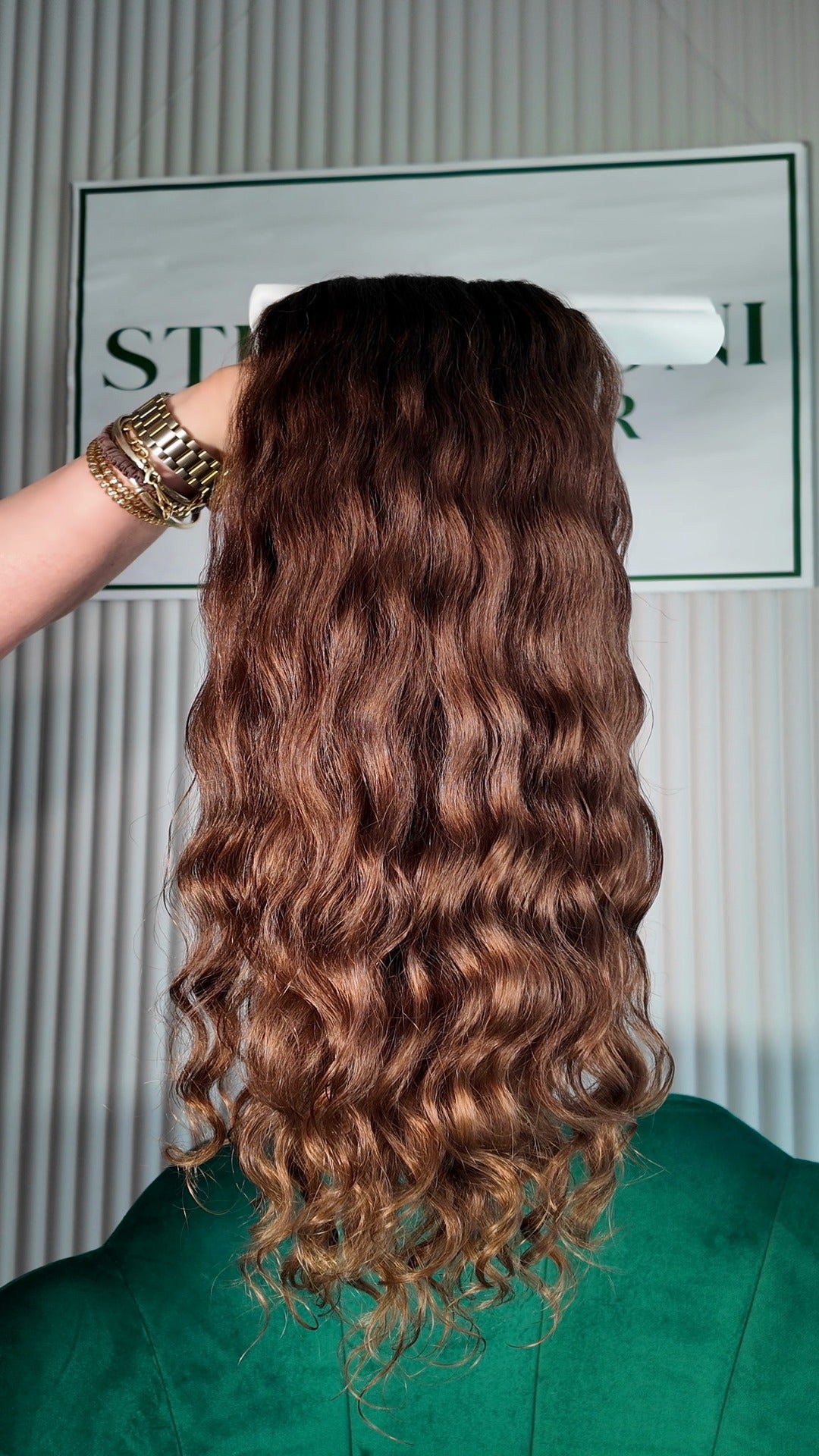 20 inch Russian single donor virgin hair tail in natural brown ombre, held up against the Stevi Pisoni Virgin Hair backdrop