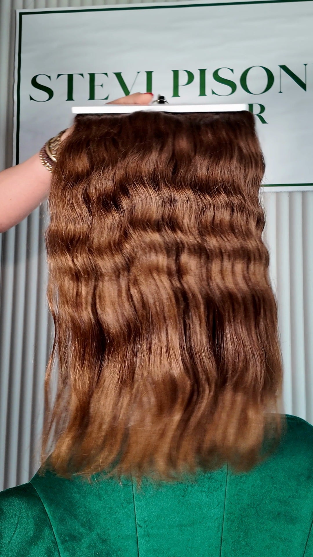 24 inch Russian single donor virgin hair tail in chestnut brown, held up against the Stevi Pisoni Virgin Hair backdrop