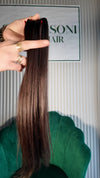 17 inch Russian single donor virgin hair tail in natural black / dark brown silky, held up against the Stevi Pisoni Virgin Hair backdrop