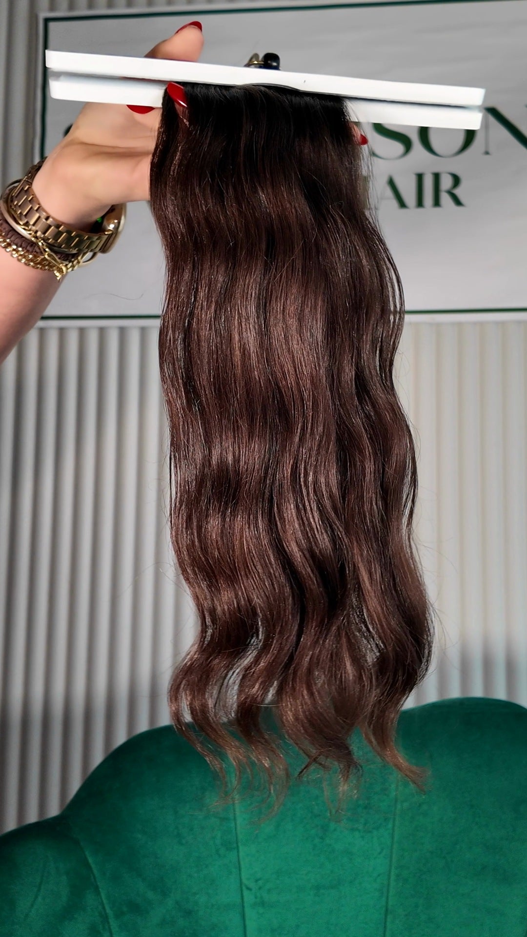 18 inch Russian single donor virgin hair tail in dark brown, held up against the Stevi Pisoni Virgin Hair backdrop