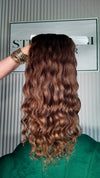 20 inch Russian single donor virgin hair tail in natural brown ombre, held up against the Stevi Pisoni Virgin Hair backdrop