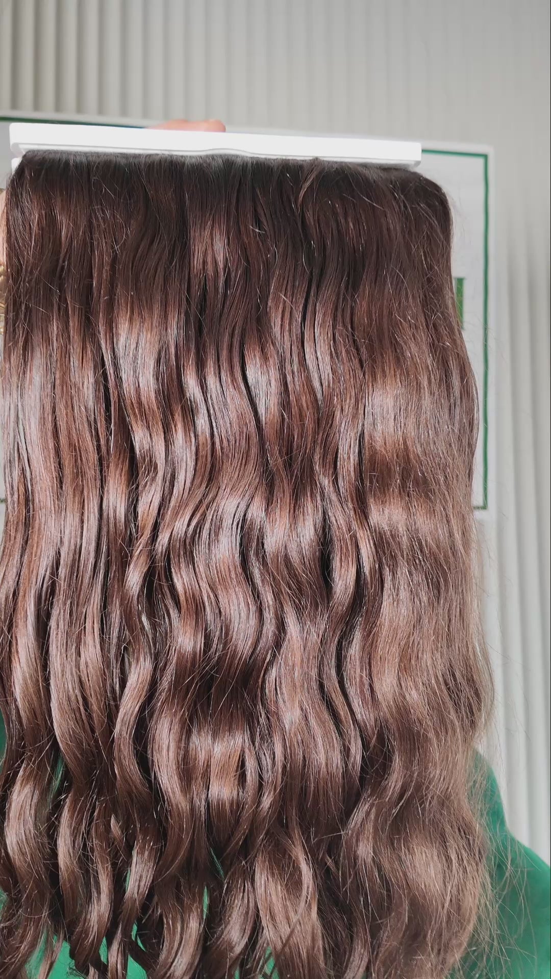 23 inch Russian single donor virgin curly mid brown hair tail held against the Stevi Pisoni Virgin Hair backdrop