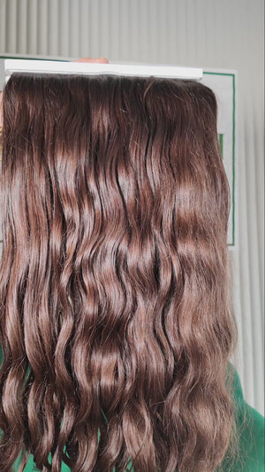 23 inch Russian single donor virgin curly mid brown hair tail held against the Stevi Pisoni Virgin Hair backdrop