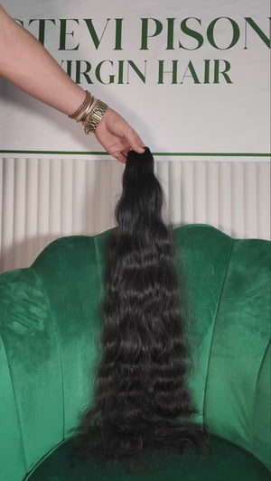 27 inch Russian single donor black virgin wavy hair tail held against the Stevi Pisoni Virgin Hair backdrop