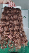 21 inch Russian single donor virgin curly light brown hair tail held against the Stevi Pisoni Virgin Hair backdrop