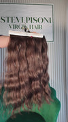19 inch Russian single donor virgin hair tail in natural black / dark brown, held up against the Stevi Pisoni Virgin Hair backdrop