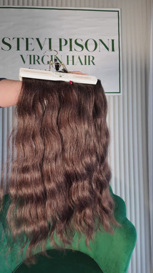 19 inch Russian single donor virgin hair tail in natural black / dark brown, held up against the Stevi Pisoni Virgin Hair backdrop